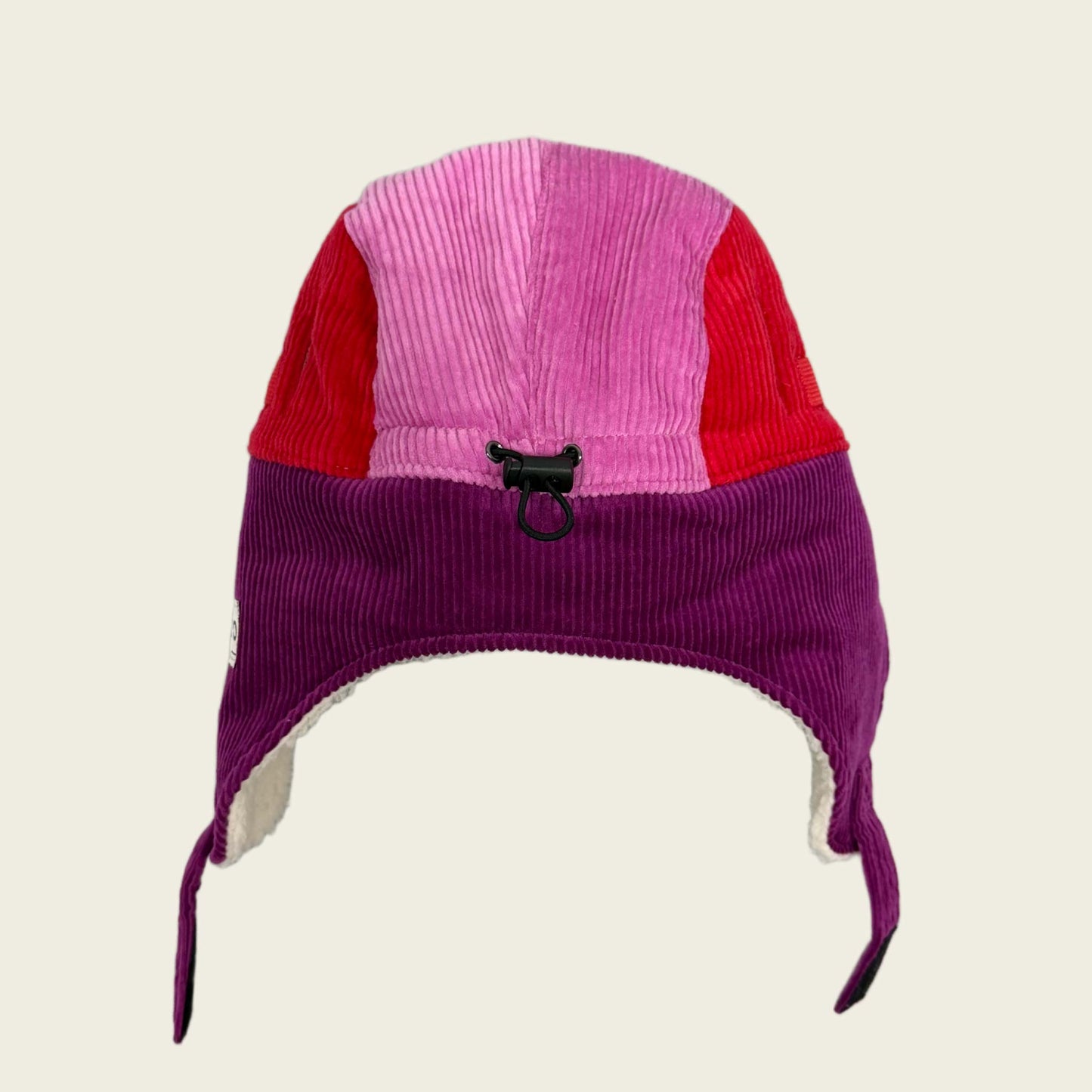 Purple and pink winter hat with earflaps on a beige background