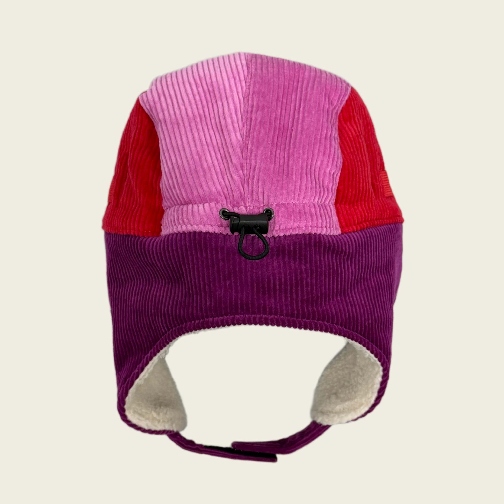 Two-tone pink and purple ear flap hat with a black toggle on a beige background