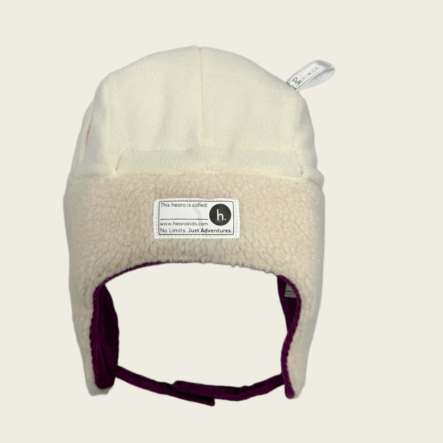Beige fleece-lined winter hat with a name label on a beige background