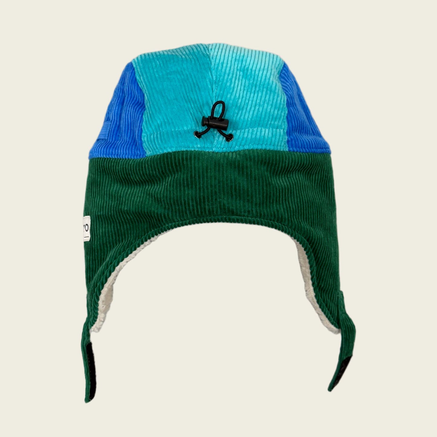 Corduroy ear flap hat with blue and green sections on a beige background