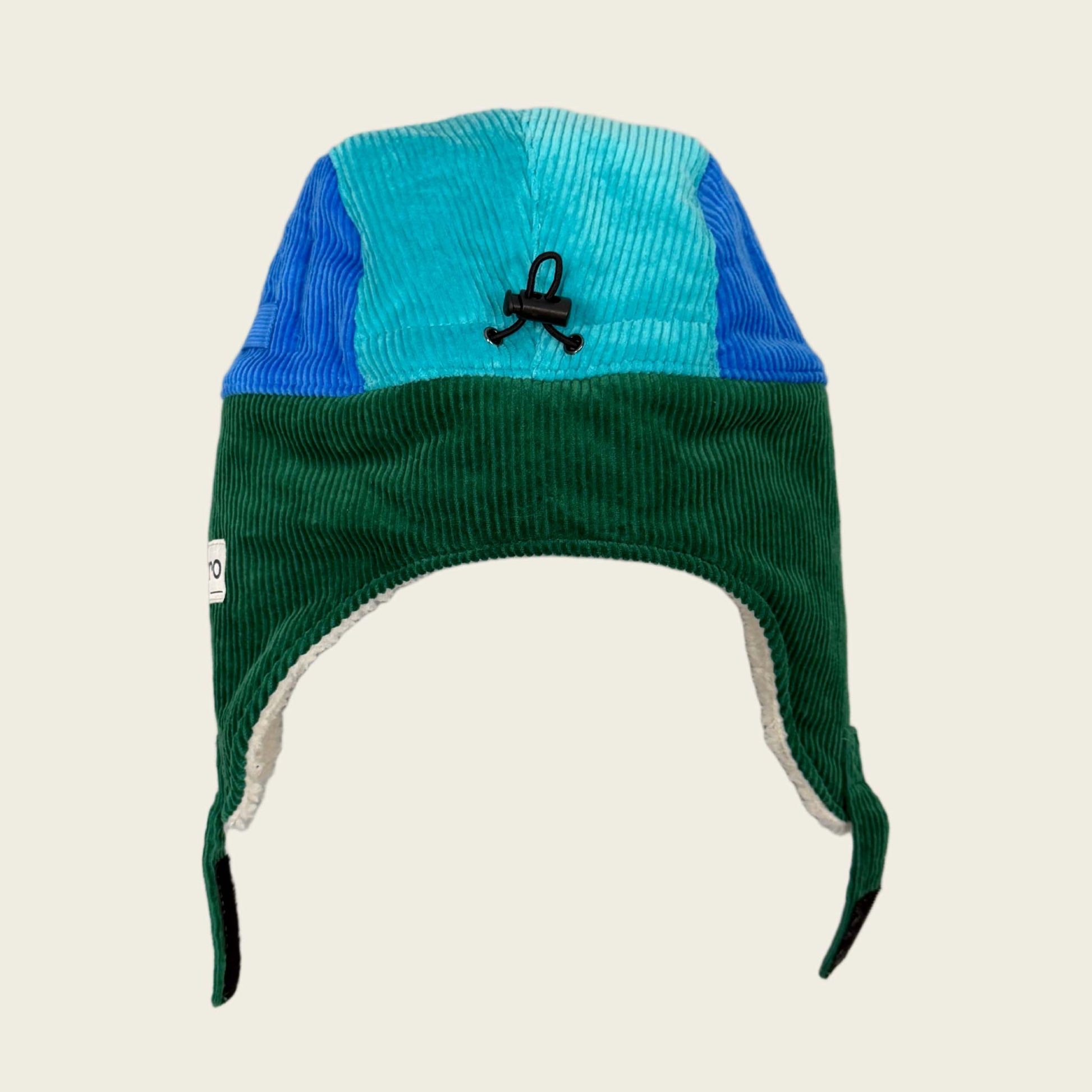 Corduroy ear flap hat with blue and green sections on a beige background