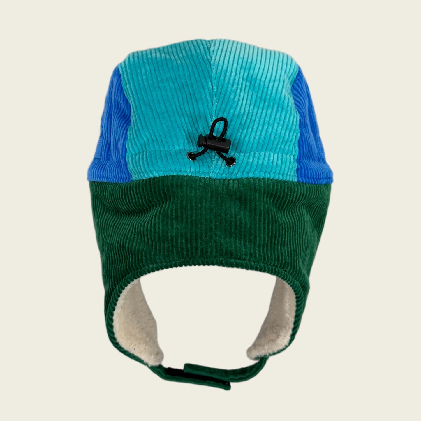 Two-tone blue and green knitted hat with earflaps on a beige background