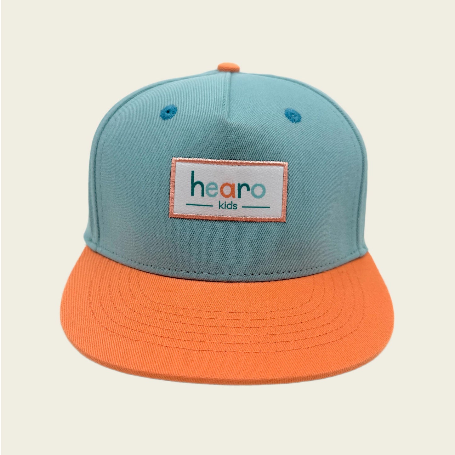 A two-tone snapback cap for kids with a light teal crown and a bright orange flat brim. The front of the cap features a rectangular patch with the text 'hearo kids' in orange and teal lettering.