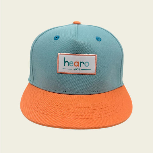 A two-tone snapback cap for kids with a light teal crown and a bright orange flat brim. The front of the cap features a rectangular patch with the text 'hearo kids' in orange and teal lettering.