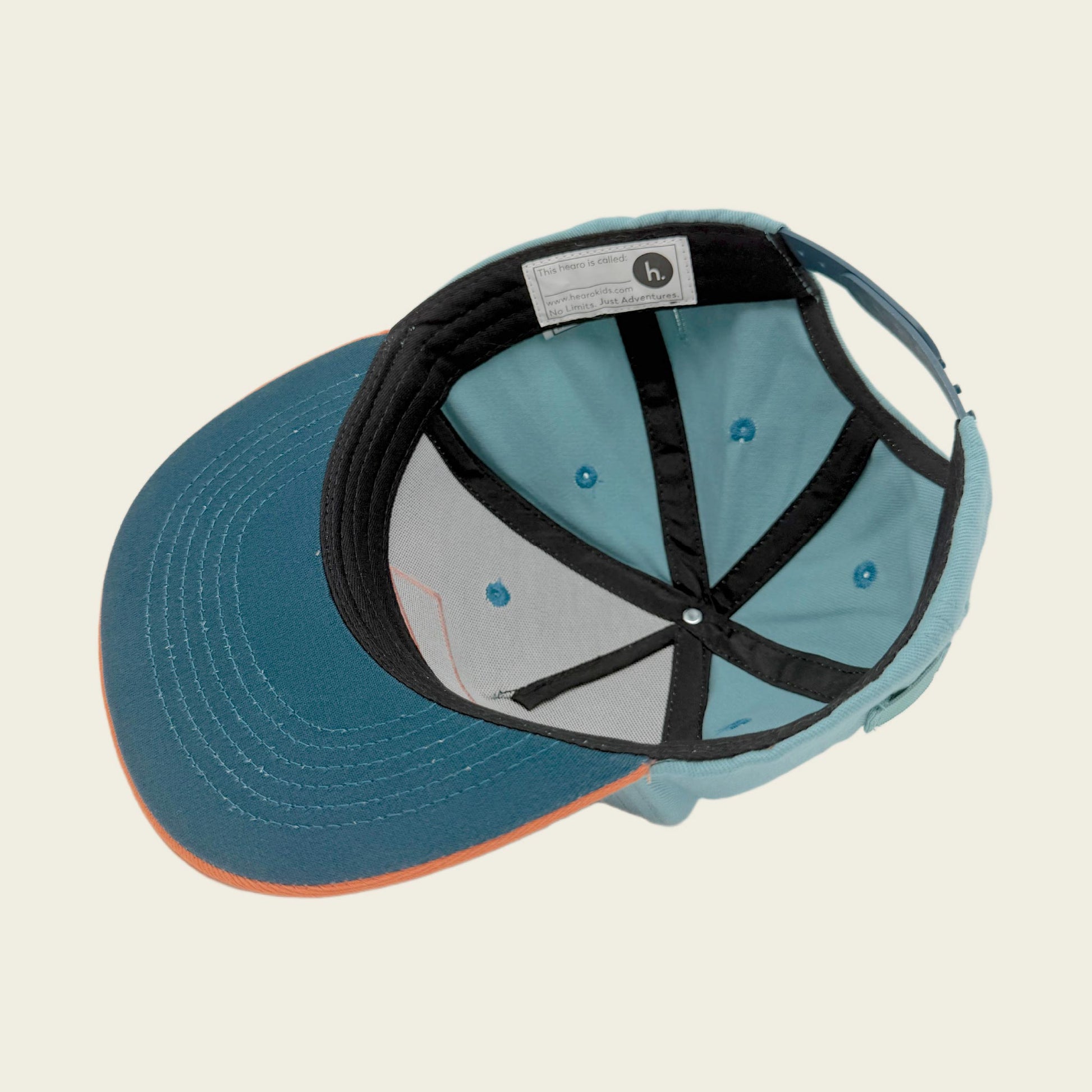 A snapback cap shown from an overhead angle, featuring a teal blue visor, a light teal crown, black internal straps, and a small orange accent along the edge of the visor.