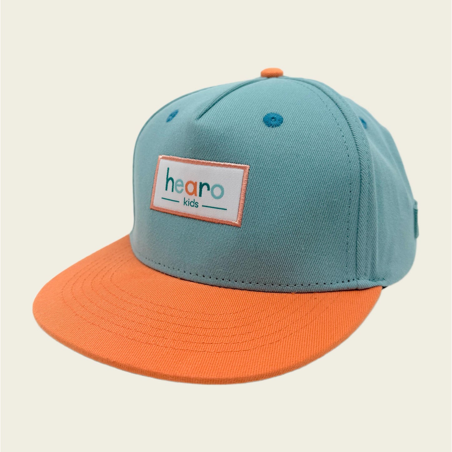 A two-tone snapback cap for kids with a light teal crown and a bright orange flat brim. The front features a white rectangular patch with the text 'hearo kids' in orange and teal.